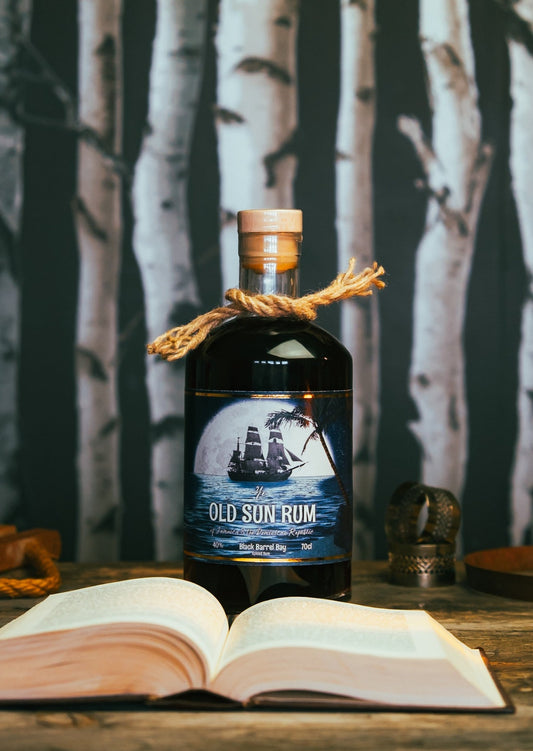 A bottle of black barrel bay behind an open book on a wooden desk