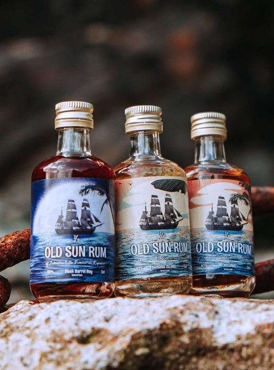 three miniature old sun rum bottles sitting on a rock in front of an anchor chain