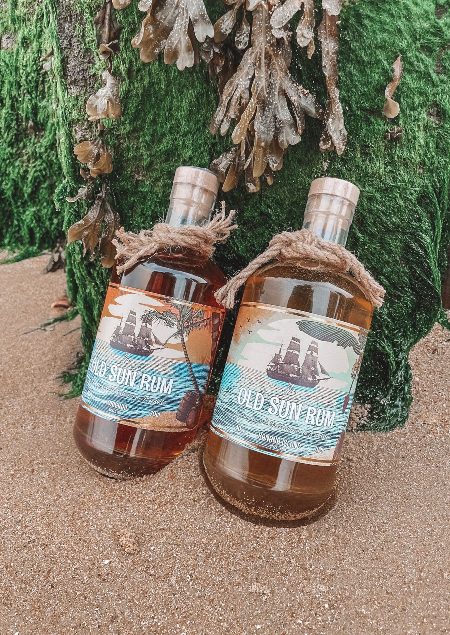 two old sun rum bottles sitting in the beach sand in front of a seaweed covered wooden block